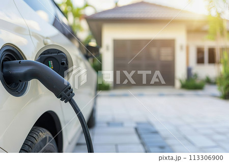An electric car plugged in and charging at a residential driveway. EV charging An electric car plugged in and charging at a residential driveway. EV charging 113306900