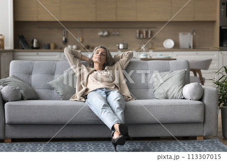 Carefree woman lying relaxing on couch in living room Carefree woman lying relaxing on couch in living room 113307015