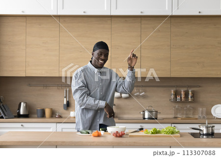 Cheerful African man dancing in the kitchen while preparing food 113307088