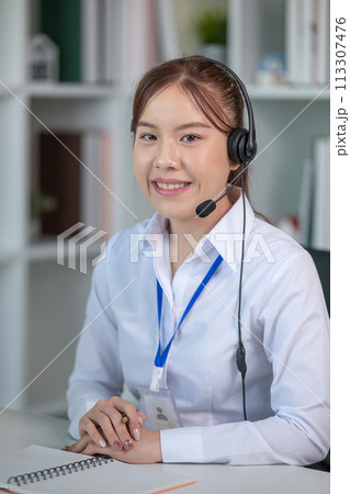 Portrait of happy smiling female customer support phone operator at workplace. Asian Portrait of happy smiling female customer support phone operator at workplace. Asian 113307476