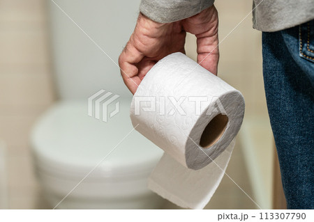 An older man's hand holding a roll of toilet paper in front of the toilet. 113307790