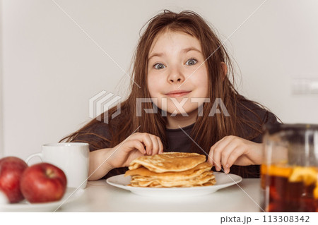 Little cheerful teenage girl preparing to eat a stack of pancakes for breakfast. High quality photo 113308342
