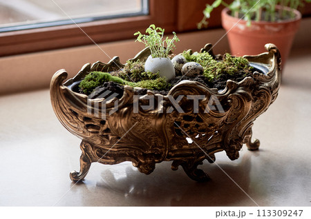A massive bronze vase on legs with moss, greenery sprouted in an egg. A new life 113309247