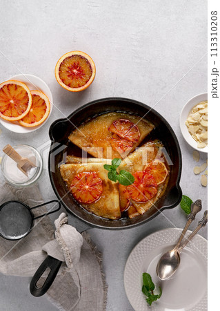 Crepes with Orange Sauce in a cast iron pan. Traditional French crepe Suzette with orange sauce. Flat lay, top view, copy space 113310208
