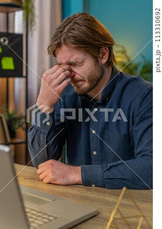 Bored sleepy businessman worker working on laptop rubbing eye pinch nose, pain headache at office Bored sleepy businessman worker working on laptop rubbing eye pinch nose, pain headache at office 113310692