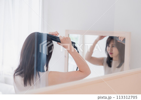 ヘアアイロンを使って髪をセットする若い女性 ヘアアイロンを使って髪をセットする若い女性 113312705