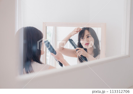 ヘアアイロンを使って髪をセットする若い女性 ヘアアイロンを使って髪をセットする若い女性 113312706
