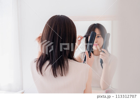 ヘアアイロンを使って髪をセットする若い女性 ヘアアイロンを使って髪をセットする若い女性 113312707