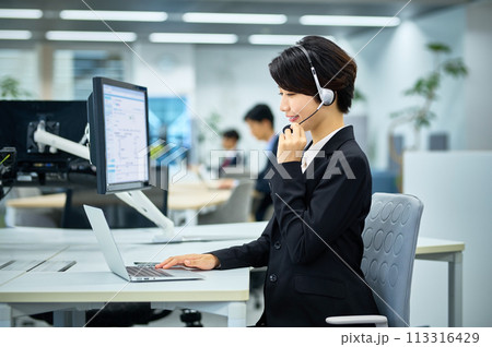 オフィスでヘットセットを付けて対応する若い女性オペレーター 113316429