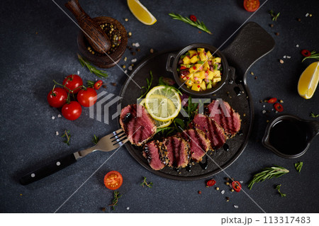 Sliced Organic grilled Tuna fillet covered with sesame seeds and mango salsa on black ceramic serving board Sliced Organic grilled Tuna fillet covered with sesame seeds and mango salsa on black ceramic serving board 113317483