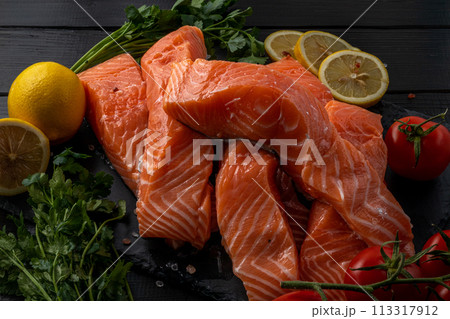 Fresh raw salmon fillet with cooking ingredients, herbs and lemon on black slate Fresh raw salmon fillet with cooking ingredients, herbs and lemon on black slate 113317912