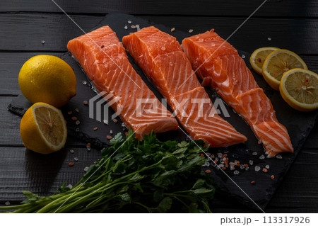 Fresh raw salmon fillet with cooking ingredients, herbs and lemon on black slate 113317926