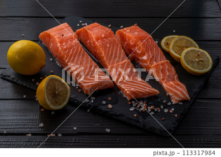 Fresh raw salmon fillet with cooking ingredients, herbs and lemon on black slate 113317984