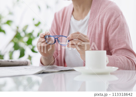 老眼鏡を手に新聞を読むミドル女性の手元 113318642