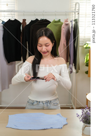 Young business woman takes a photo of a cloth with her smartphone device to put it up for sale on a second-hand clothing platform. online selling concept Young business woman takes a photo of a cloth with her smartphone device to put it up for sale on a second-hand clothing platform. online selling concept 113321760