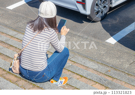 駐車場の階段で座ってスマートフォンを操作する女性 113321823