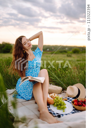Young woman sits on a plaid with a book. Summer picnic in nature. Healthy food. Young woman sits on a plaid with a book. Summer picnic in nature. Healthy food. 113322394