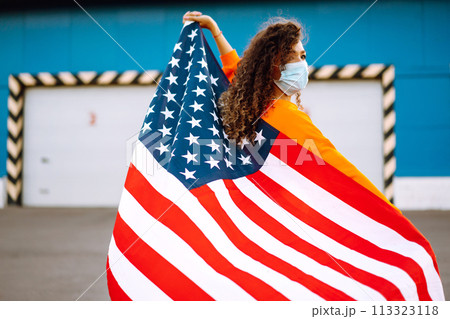 African American woman with medical face mask posing with american flag.The concept of preventing the spread of the epidemic. Covid-2019. 113323118