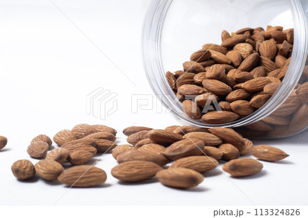 Almonds falling from a glass container leaning against a white background Almonds falling from a glass container leaning against a white background 113324826