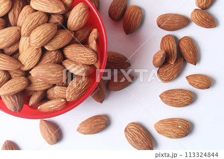 Almonds in a red bowl on a white background and scattered around it. closeup Almonds in a red bowl on a white background and scattered around it. closeup 113324844