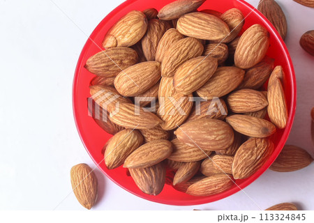Close up of almonds in a red bowl on a white background. Close up of almonds in a red bowl on a white background. 113324845