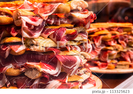Traditional Spanish bocadillos with Iberico jamon laid out in a slide on a shop window 113325623