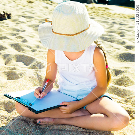 Child girl in hat writes draws dreams with sand on seashore 113325659
