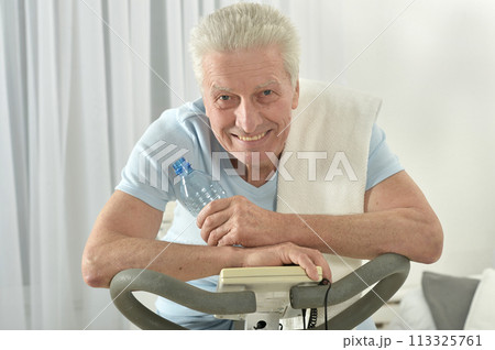 An elderly man is exercising on an exercise bike 113325761