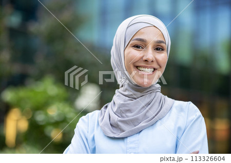 Portrait of a joyful young woman wearing a hijab, with a modern city background. Emphasizing diversity and happiness. 113326604