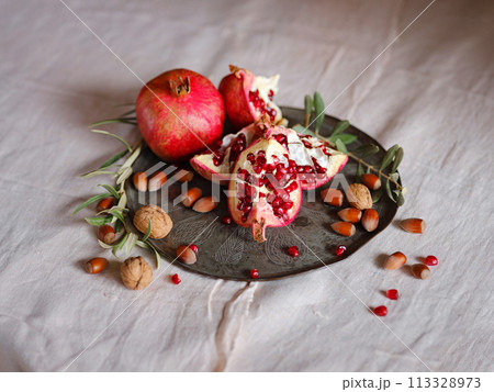 Image of Still Life with Turkish Pomegranate and olive branch on old retro plate. Dark wood background, antique copper plate. Fresh ripe whole pomegranates, opened pomegranate and seeds 113328973
