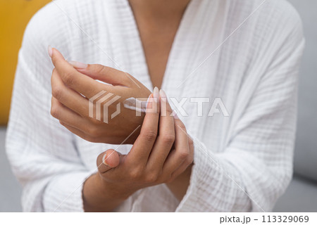 Self-pampering: In her bathrobe, a woman relishes a body skincare ritual, applying moisturizing cream to her hand in a close-up. Self-pampering: In her bathrobe, a woman relishes a body skincare ritual, applying moisturizing cream to her hand in a close-up. 113329069