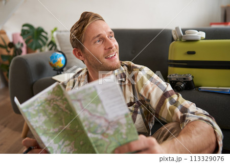 Handsome smiling tourist, man holds map, plans his holiday, going on vacation, looking aside with dreamy, happy face expression Handsome smiling tourist, man holds map, plans his holiday, going on vacation, looking aside with dreamy, happy face expression 113329076