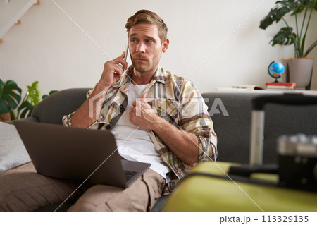 Portrait of man talking on mobile phone, tourist with laptop and suitcase answers telephone 113329135