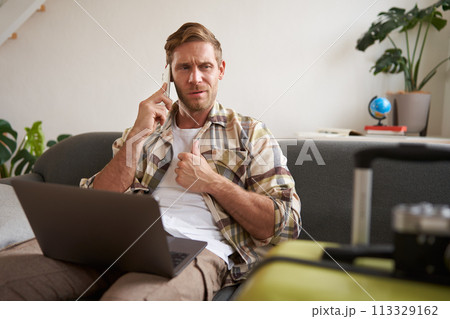 Portrait of man talking on mobile phone, tourist with laptop and suitcase answers telephone Portrait of man talking on mobile phone, tourist with laptop and suitcase answers telephone 113329162