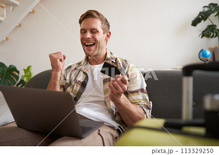 Portrait of happy man, traveller, holding credit card and using laptop, booking vacation, buying tickets online for summer holiday, has suitcase packed Portrait of happy man, traveller, holding credit card and using laptop, booking vacation, buying tickets online for summer holiday, has suitcase packed 113329250