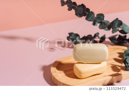 Two bars of soap in a wooden soap dish with dried flowers against a pink background Two bars of soap in a wooden soap dish with dried flowers against a pink background 113329472
