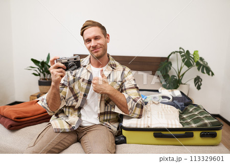 Portrait of handsome man going on vacation, packing suitcase, holding camera, travel photographer going on holiday 113329601