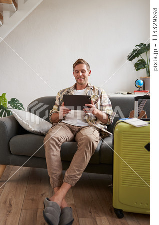 Vertical shot of man, tourist with suitcase, looking at digital tablet, reading about travel destination, booking hotel on gadget 113329698