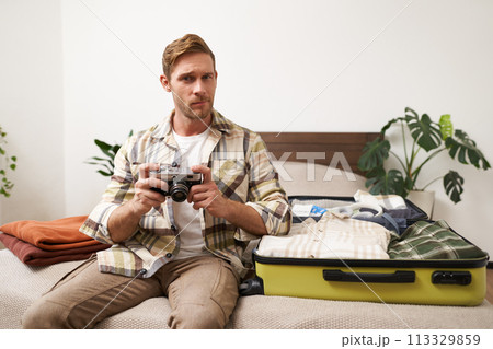 Portrait of handsome man going on vacation, packing suitcase, holding camera, travel photographer going on holiday 113329859
