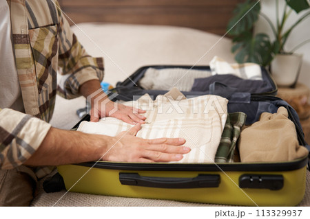 Cropped shot of male hands, tourist puts his clothes in suitcase, packs luggage for holiday trip, goes on vacation 113329937
