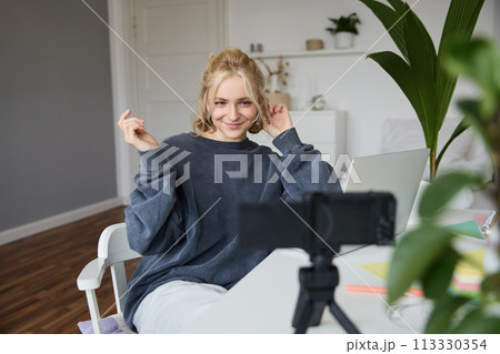 Portrait of young woman, lifestyle blogger, recording vlog video about her life and daily routine, sitting in front of laptop, talking to followers, sitting in her room Portrait of young woman, lifestyle blogger, recording vlog video about her life and daily routine, sitting in front of laptop, talking to followers, sitting in her room 113330354
