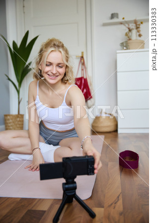 Portrait of young fitness instructor, vlogger creating content at home, doing workout and record exercises on digital camera, using rubber yoga mat Portrait of young fitness instructor, vlogger creating content at home, doing workout and record exercises on digital camera, using rubber yoga mat 113330383