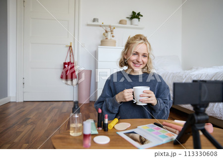 Portrait of beautiful social media beauty blogger, sitting in front of digital camera on floor in bedroom, drinking tea and chatting, talking to followers Portrait of beautiful social media beauty blogger, sitting in front of digital camera on floor in bedroom, drinking tea and chatting, talking to followers 113330608