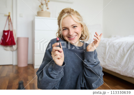 Portrait of cute, charismatic beauty blogger, woman sits in a room with lipstick in hand, talking about makeup, chatting with followers, recording online stream on social media app Portrait of cute, charismatic beauty blogger, woman sits in a room with lipstick in hand, talking about makeup, chatting with followers, recording online stream on social media app 113330639