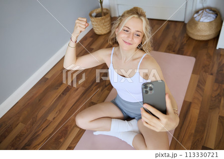 Portrait of young sporty woman taking selfie during workout training, content creator takes photos, shows muscles on camera, flexing biceps Portrait of young sporty woman taking selfie during workout training, content creator takes photos, shows muscles on camera, flexing biceps 113330721