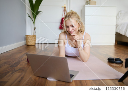 Portrait of beautiful blond woman looking at fitness video tutorials on laptop, lying on rubber yoga mat, following workout instructions online Portrait of beautiful blond woman looking at fitness video tutorials on laptop, lying on rubber yoga mat, following workout instructions online 113330756