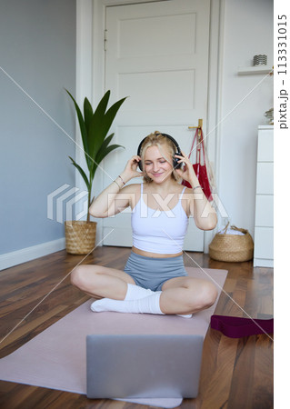 Portrait of young woman at home, connects to online gym training session, following fitness instructions on laptop, wearing wireless headphones during workout Portrait of young woman at home, connects to online gym training session, following fitness instructions on laptop, wearing wireless headphones during workout 113331015