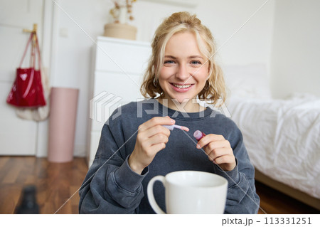 Lifestyle, beauty blogger, woman recording video of her putting on makeup, talking to camera, making online tutorial, showing her lip gloss or lipstick to followers, sitting on floor with cup of tea Lifestyle, beauty blogger, woman recording video of her putting on makeup, talking to camera, making online tutorial, showing her lip gloss or lipstick to followers, sitting on floor with cup of tea 113331251
