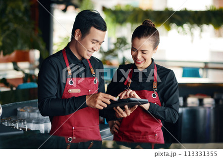 Restaurant manager teaching waiter how to use application when checking orders 113331355