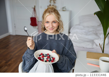 Portrait of young vlogger, content creator, showing her homemade breakfast on camera, eating dessert, smiling and looking happy 113331446
